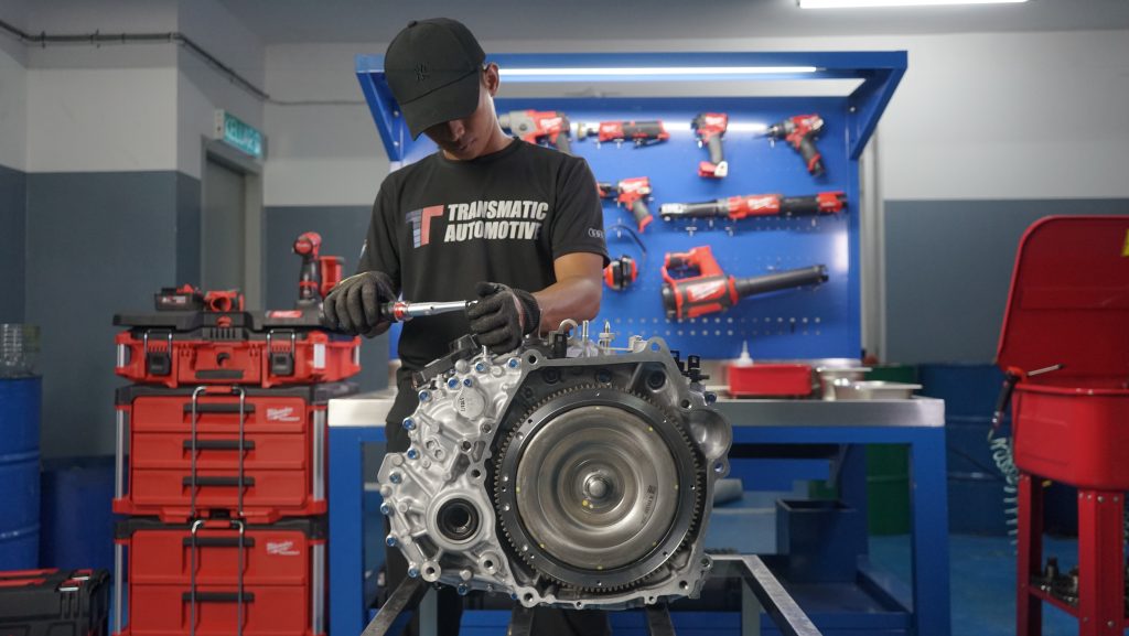 Image place on (Transmission Maintenance) page. Image showing one of our staff is currently doing maintenance towards a car gearbox with background fill with tools and equipment for repairing purposes